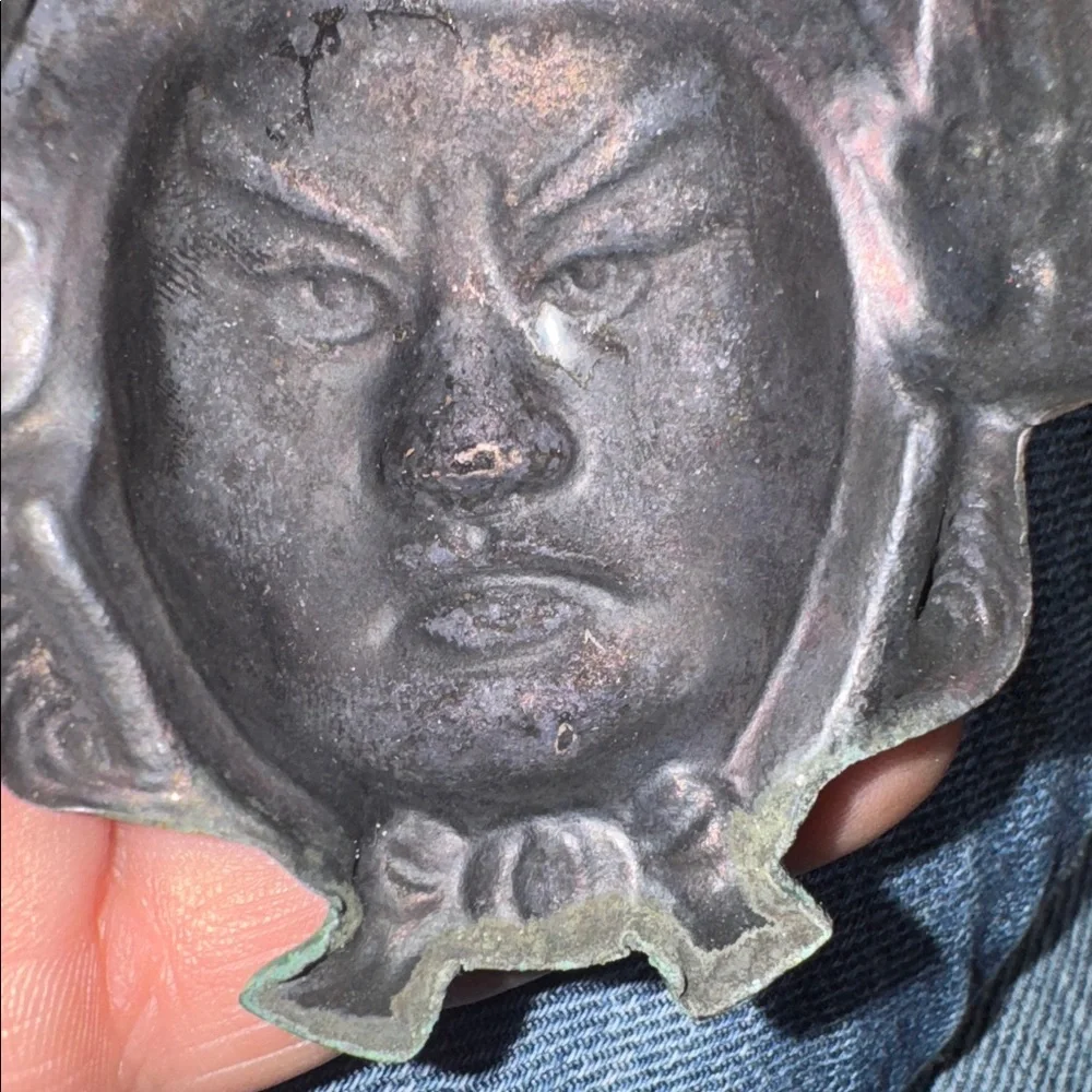 Vintage enameled metal decorative mask of an Asian man's face.